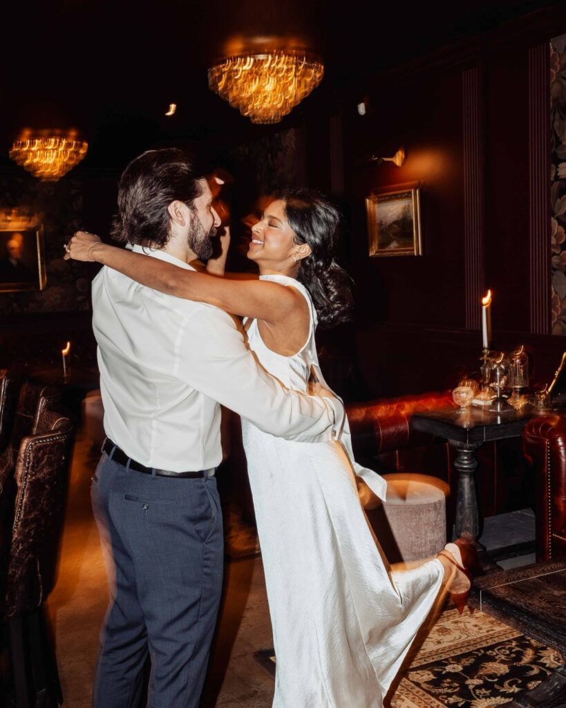 Couple embracing and smiling in a moody, elegant bar with warm chandelier lighting.