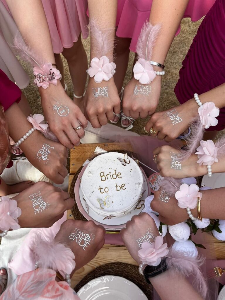 Women's hands with floral corsages surrounding a white Bride to be cake