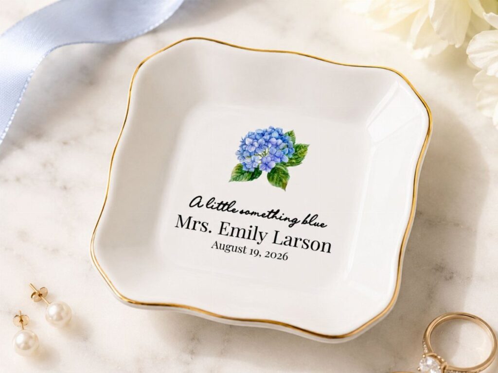 Personalized white ceramic jewelry dish with gold rim, blue flower, and bridal text.