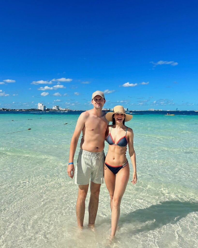 Couple in swimwear standing in turquoise ocean water on a white sand beach.