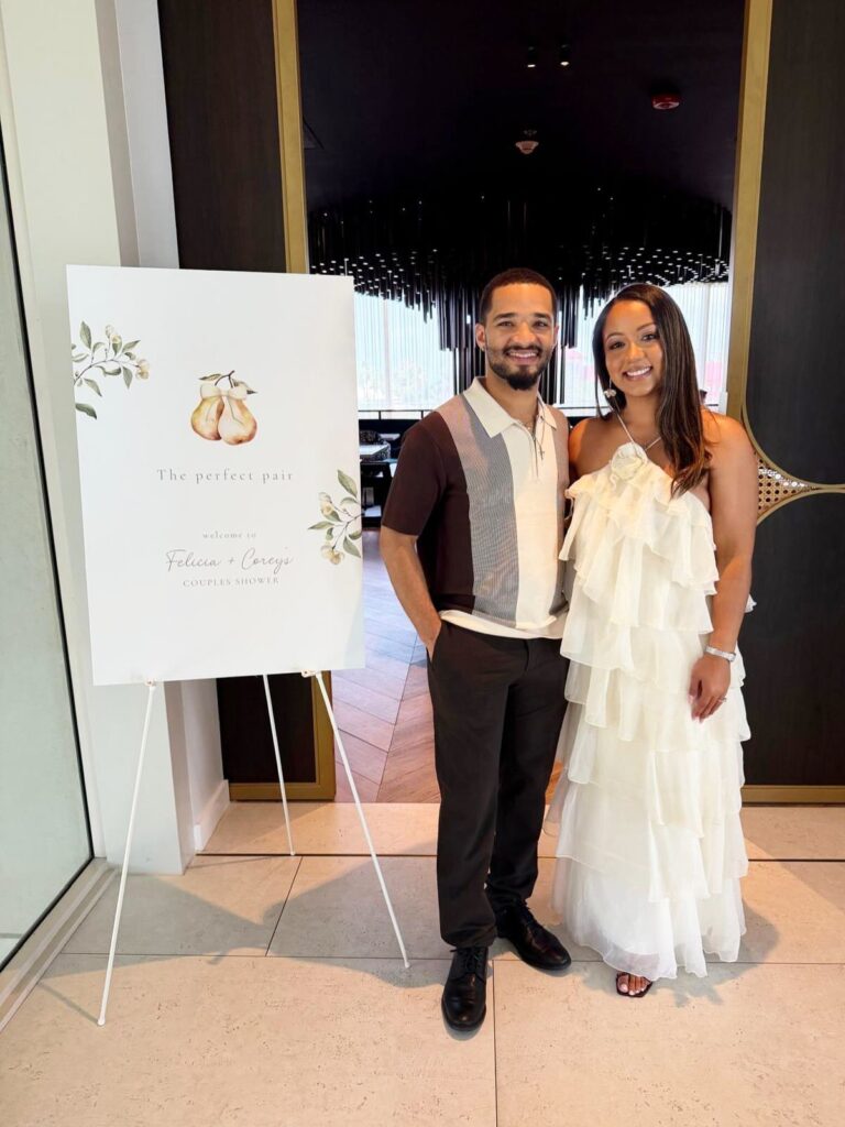 Smiling couple standing next to a white welcome sign in a modern entryway.