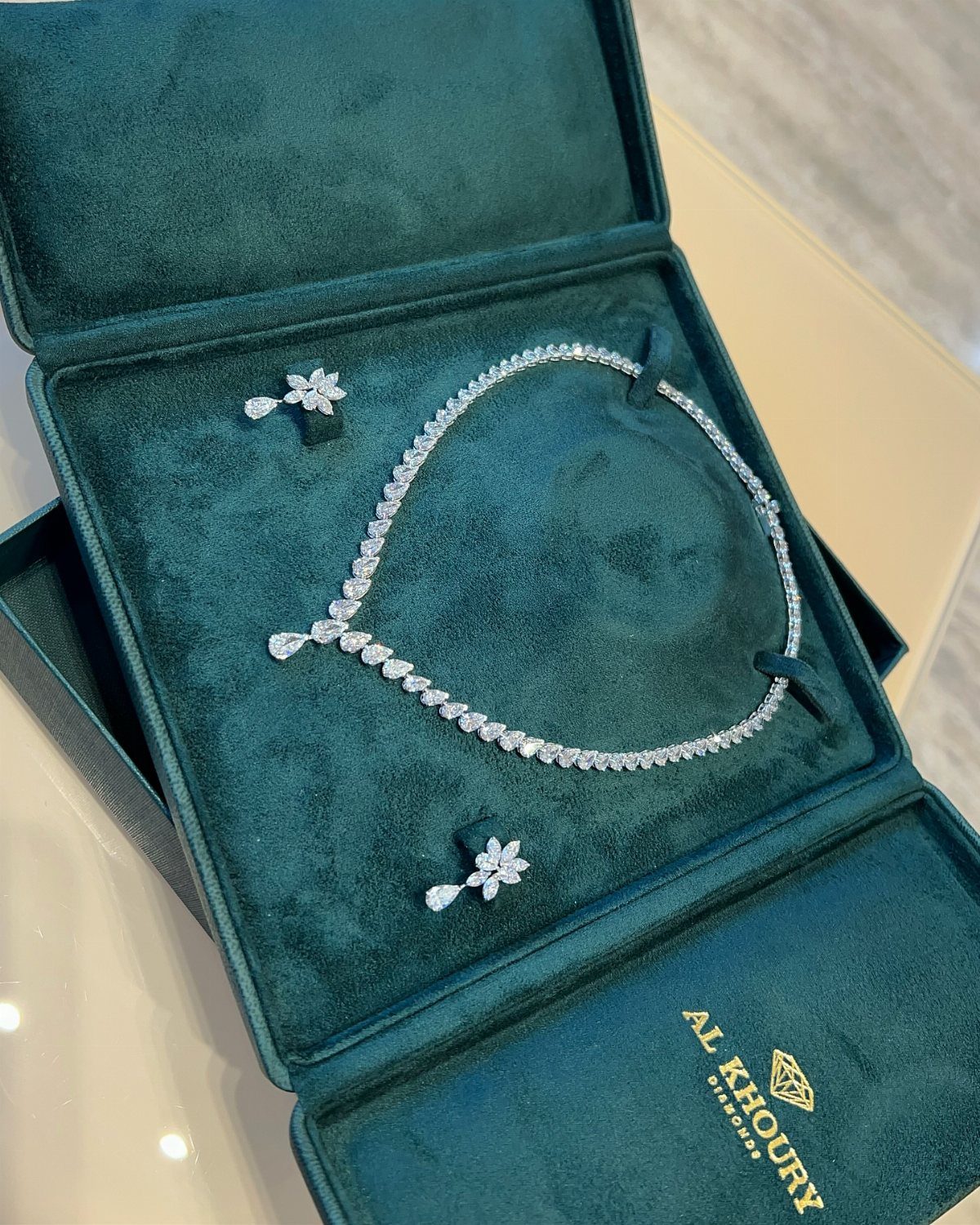 Diamond necklace and matching earrings resting in a teal velvet jewelry box