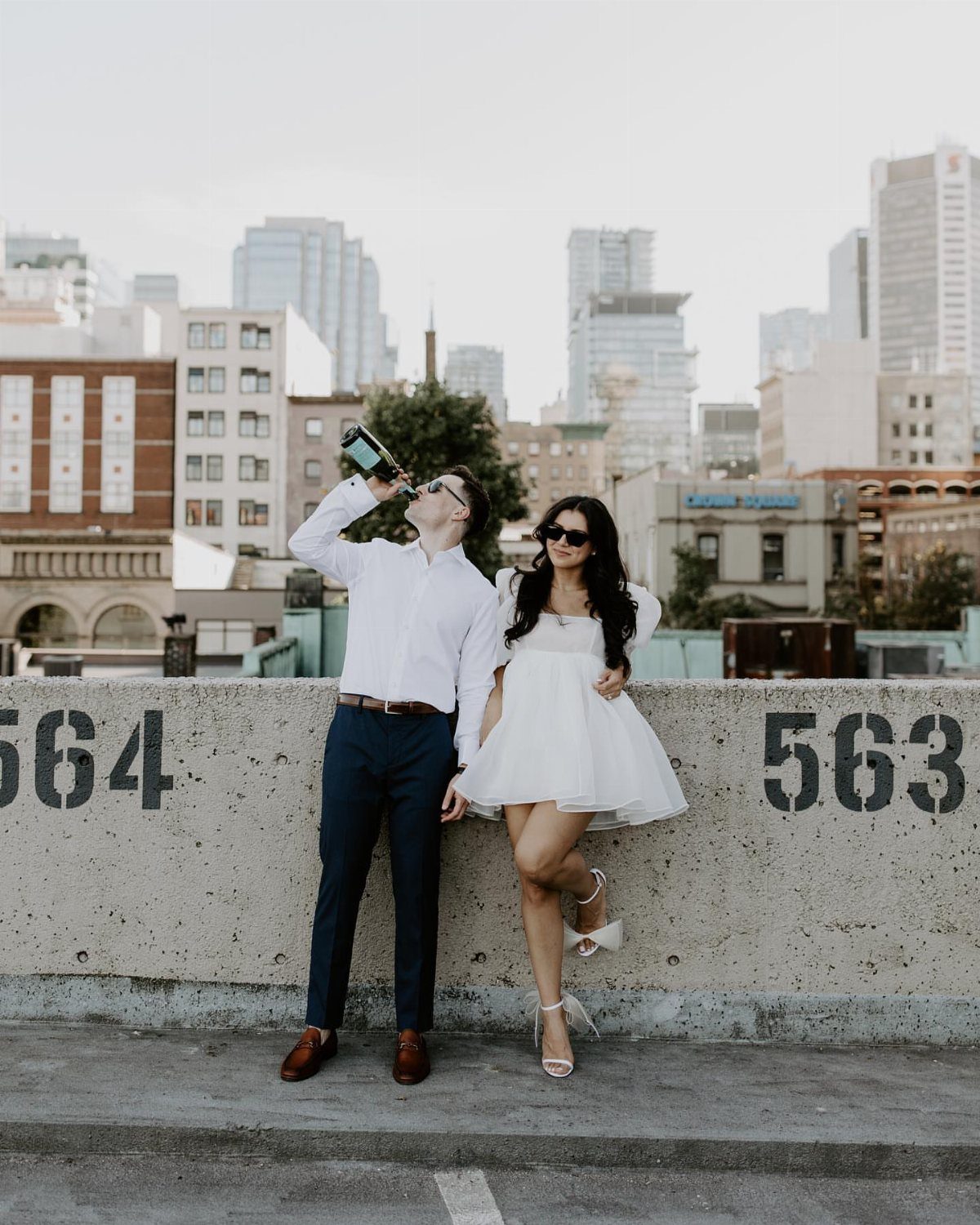 Couple posing on a city rooftop, woman wearing a short white engagement dress.