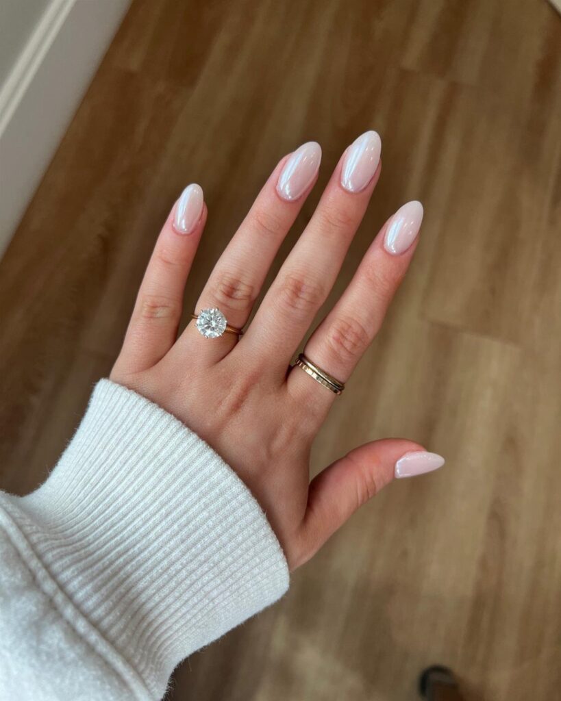 Hand with pearlescent white almond nails wearing a diamond engagement ring