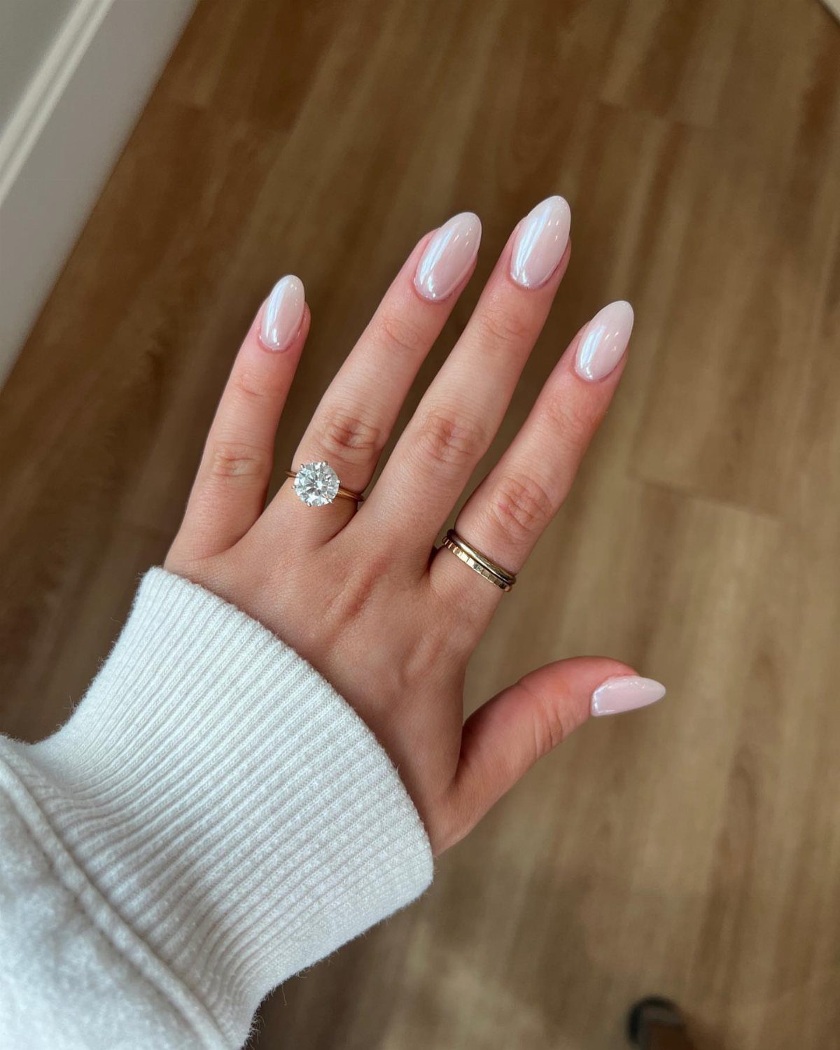Hand with pearlescent white almond nails wearing a diamond engagement ring