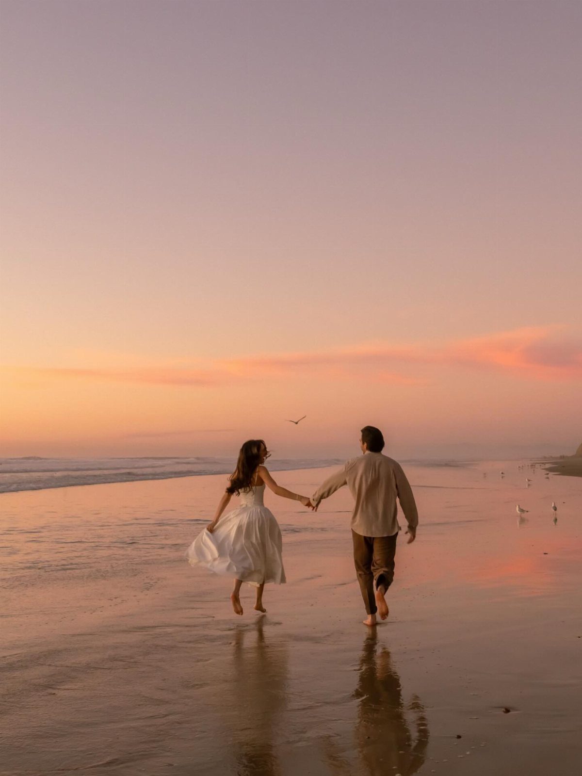 Couple holding hands walking on a beach during a sunset engagement photoshoot