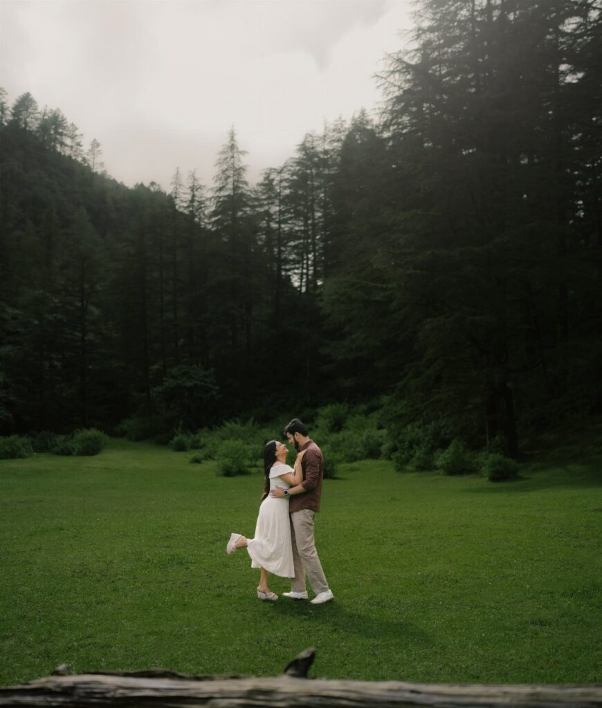 Couple embracing in a forest meadow, woman wearing a white engagement photoshoot dress.