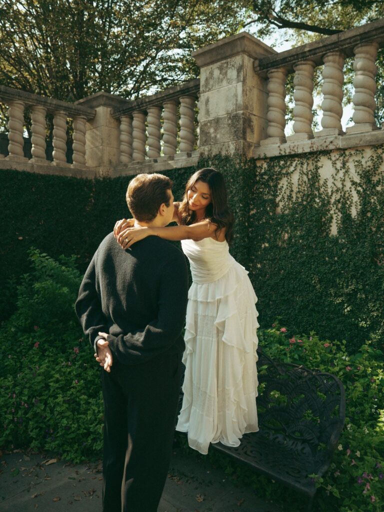 Couple embracing in a garden, woman wearing a tiered white dress and man in black.