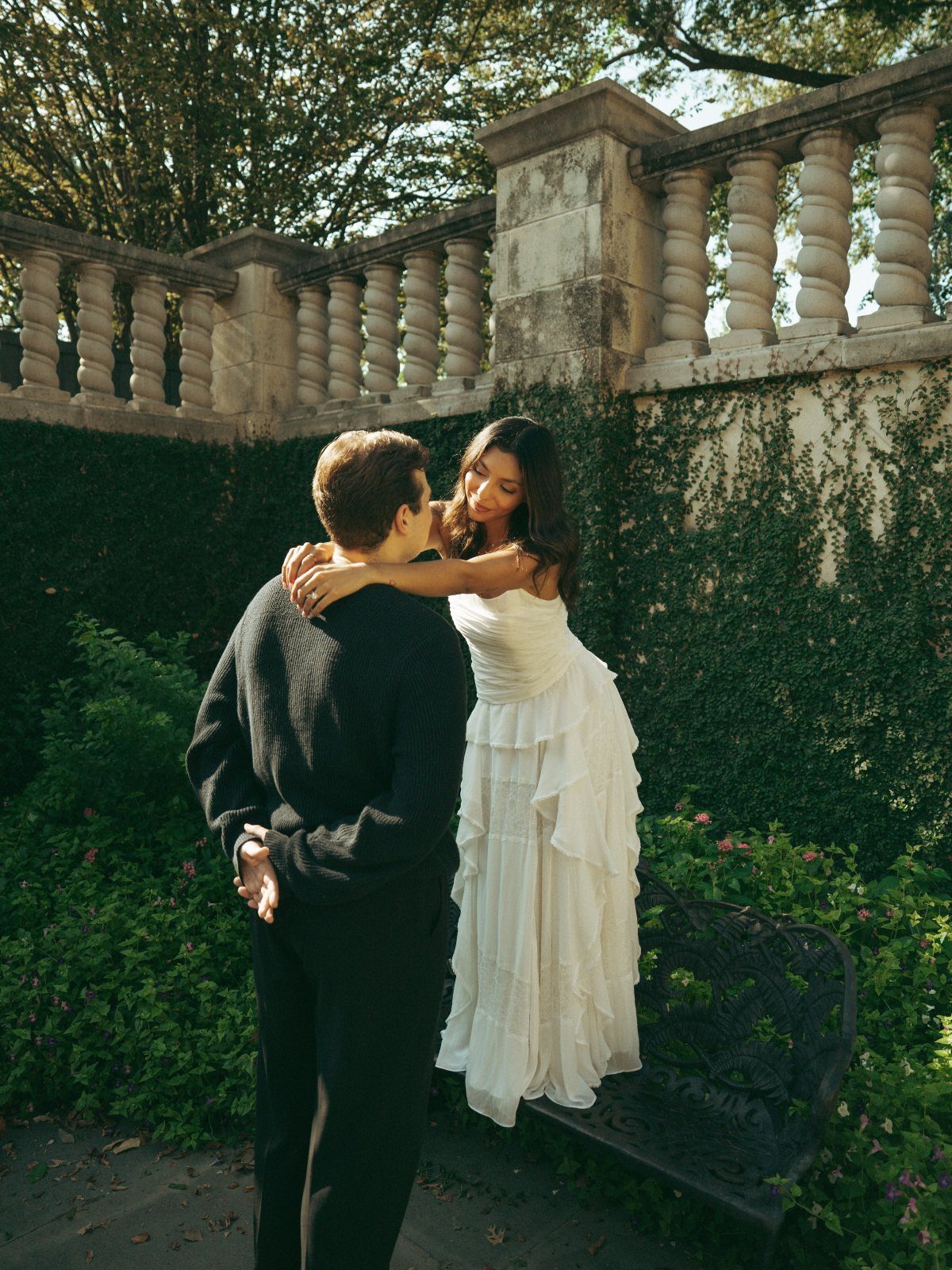 Couple embracing in a garden, woman wearing a tiered white dress and man in black.