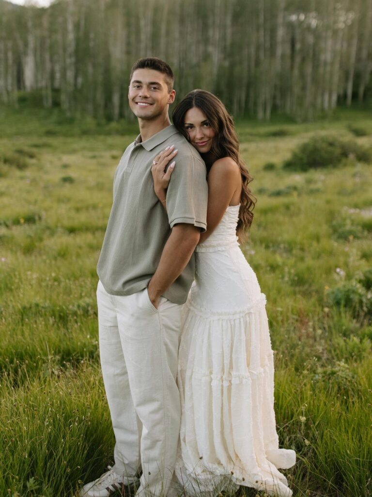 Couple posing in a field wearing a sage green shirt and white lace dress.