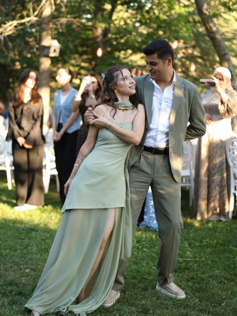 Couple in matching olive green formal attire posing together on a sunny lawn