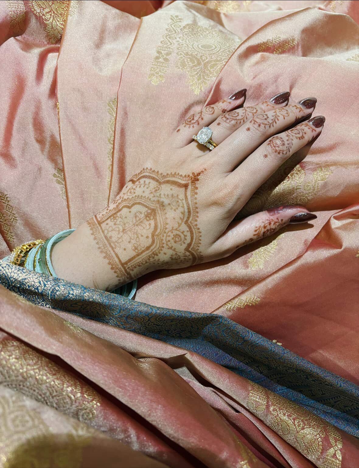 Hand with henna patterns wearing a gold diamond engagement ring on peach fabric