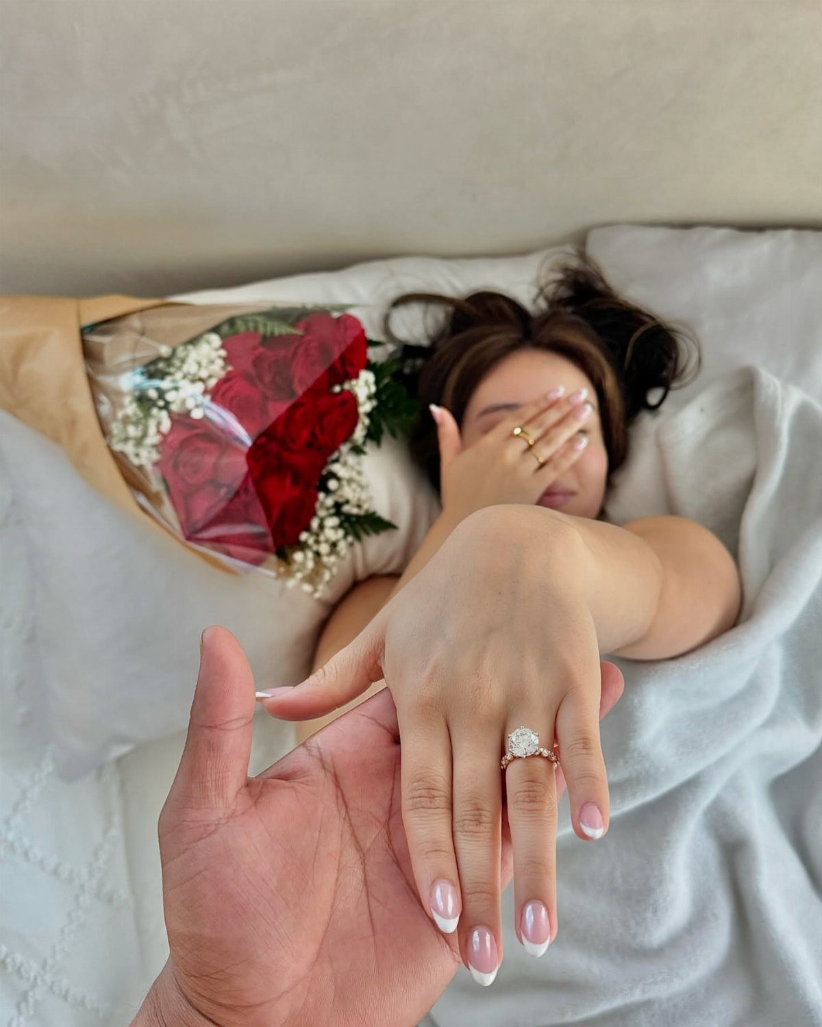 Solitaire diamond engagement ring on a woman's finger held by a man's hand.