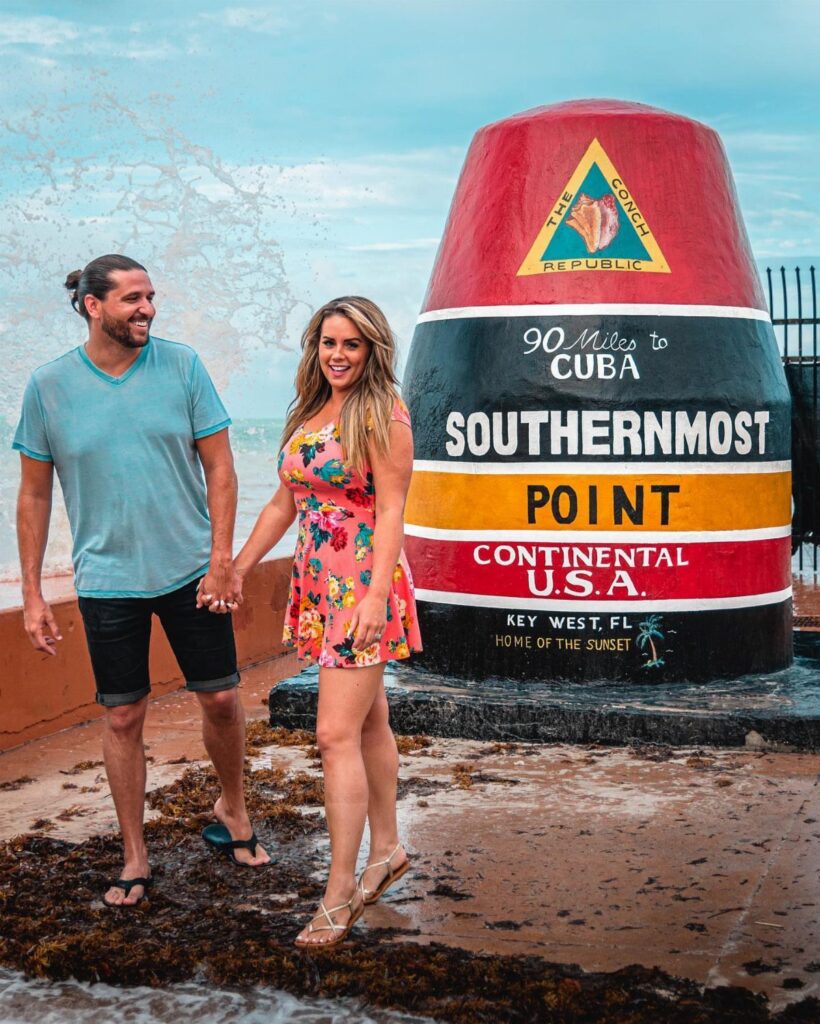 Couple holding hands next to the Southernmost Point buoy in Key West, Florida