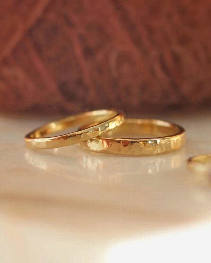 Two hammered gold wedding rings resting on a reflective white surface.