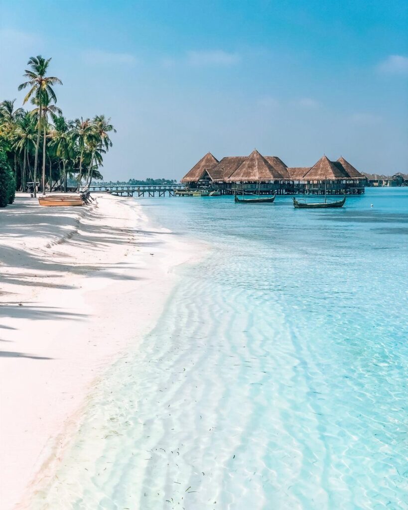 Thatched-roof overwater bungalows on a tropical beach with white sand and turquoise water.