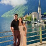Couple posing by a lake with a European village and mountains in background