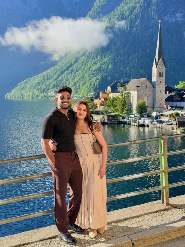 Couple posing by a lake with a European village and mountains in background