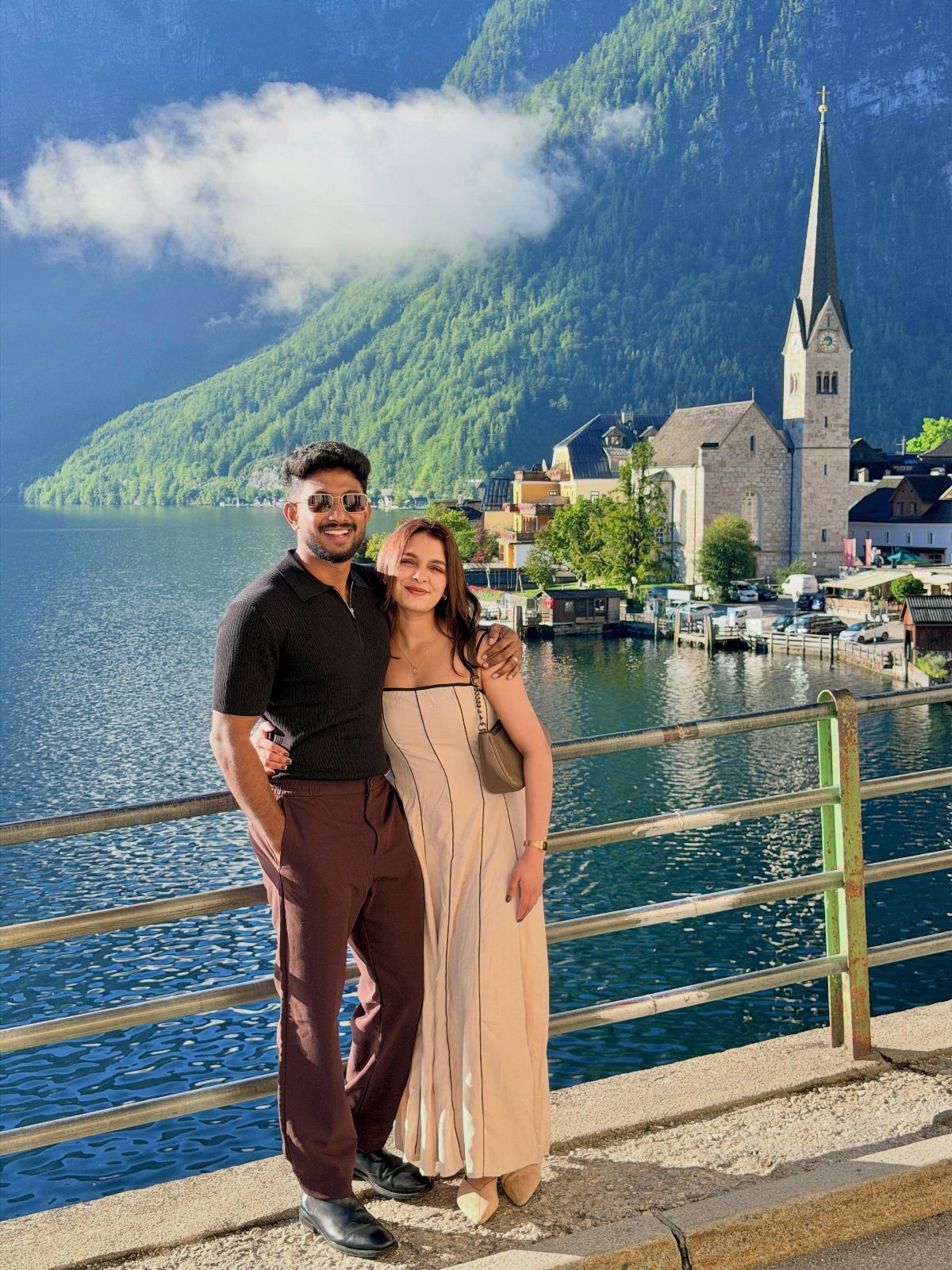 Couple posing by a lake with a European village and mountains in background