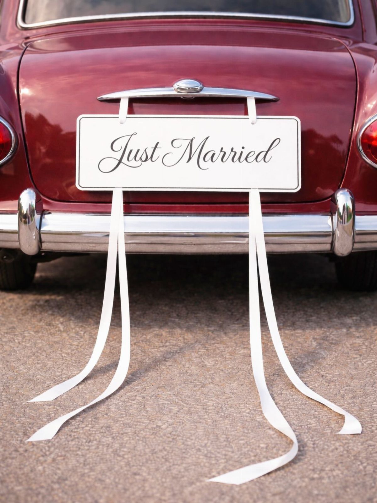Just Married sign with cursive lettering attached to the back of a red car