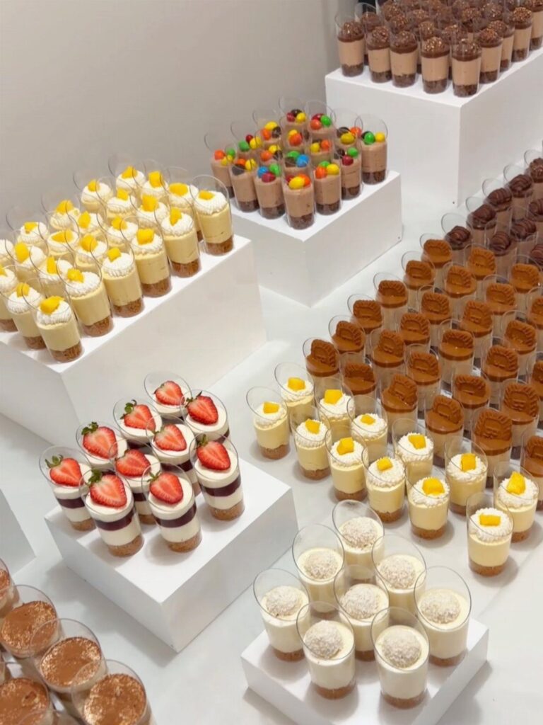 Mini dessert cups with fruit and chocolate arranged on white tiered display stands.