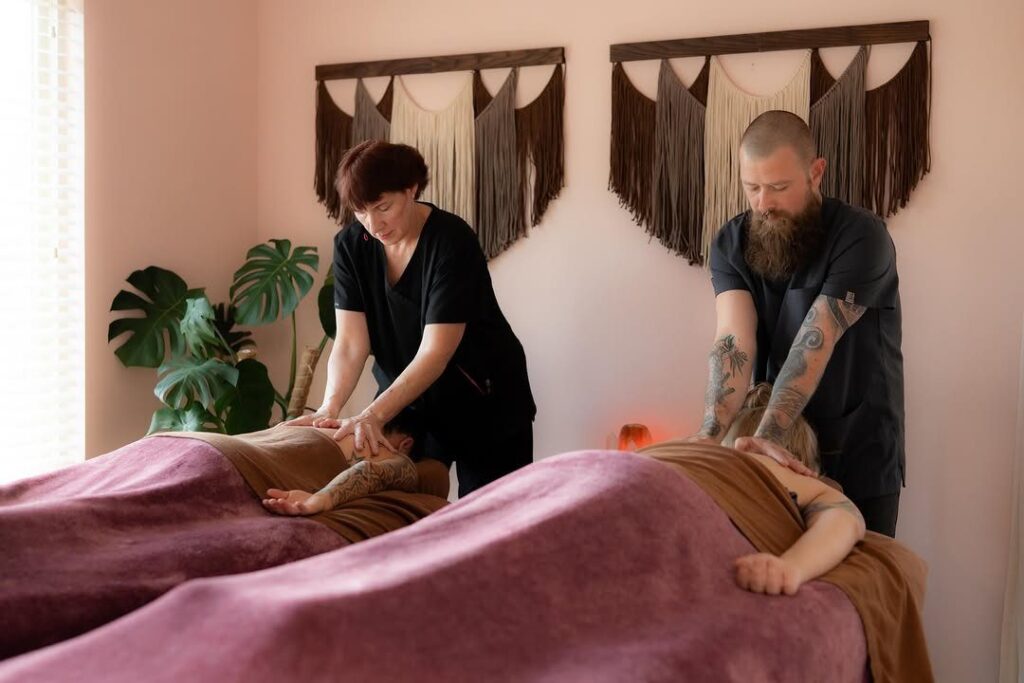 Two massage therapists giving simultaneous massages to a couple in a spa room.