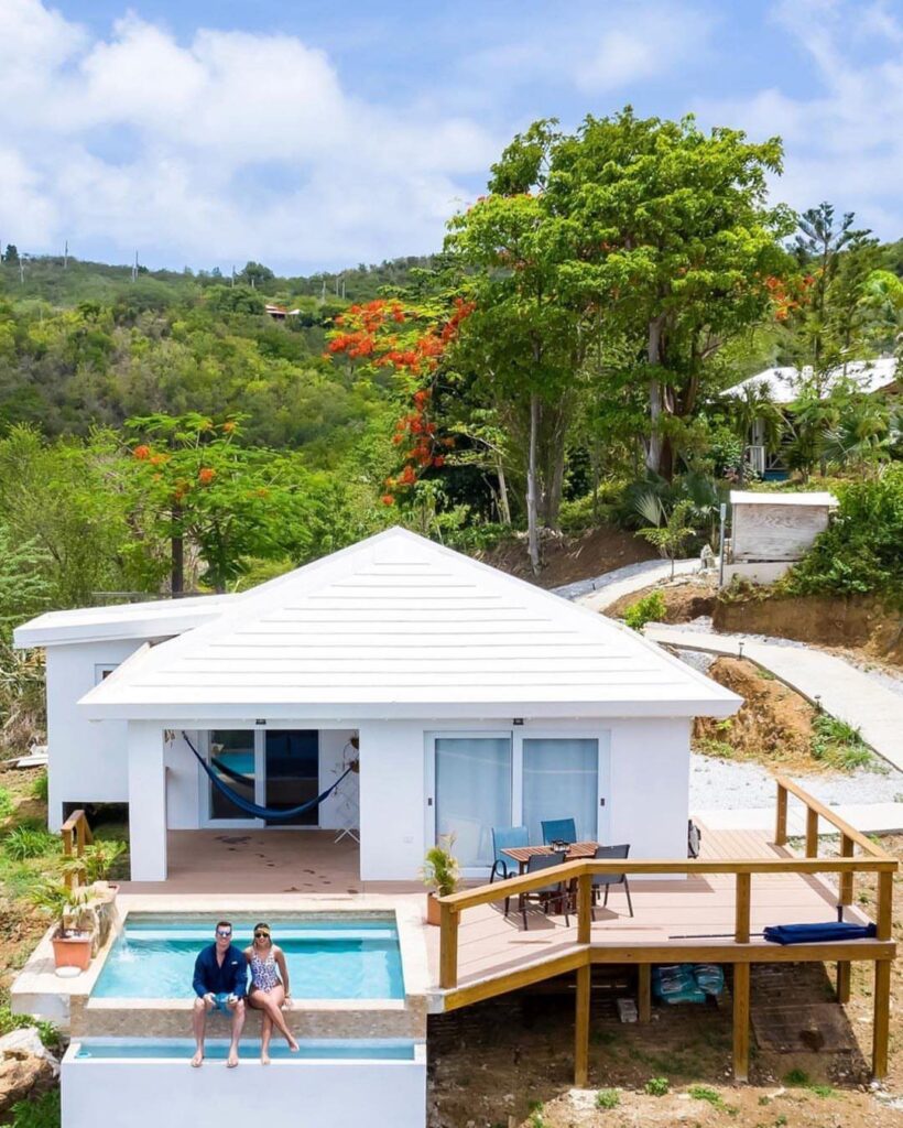Couple sitting by a pool at a white luxury villa in tropical greenery.