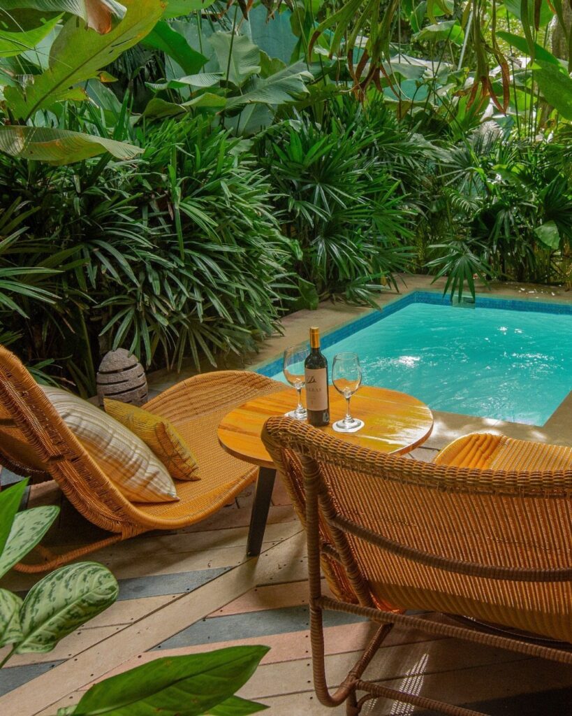 Wicker lounge chairs and wine by a private plunge pool in a tropical garden.