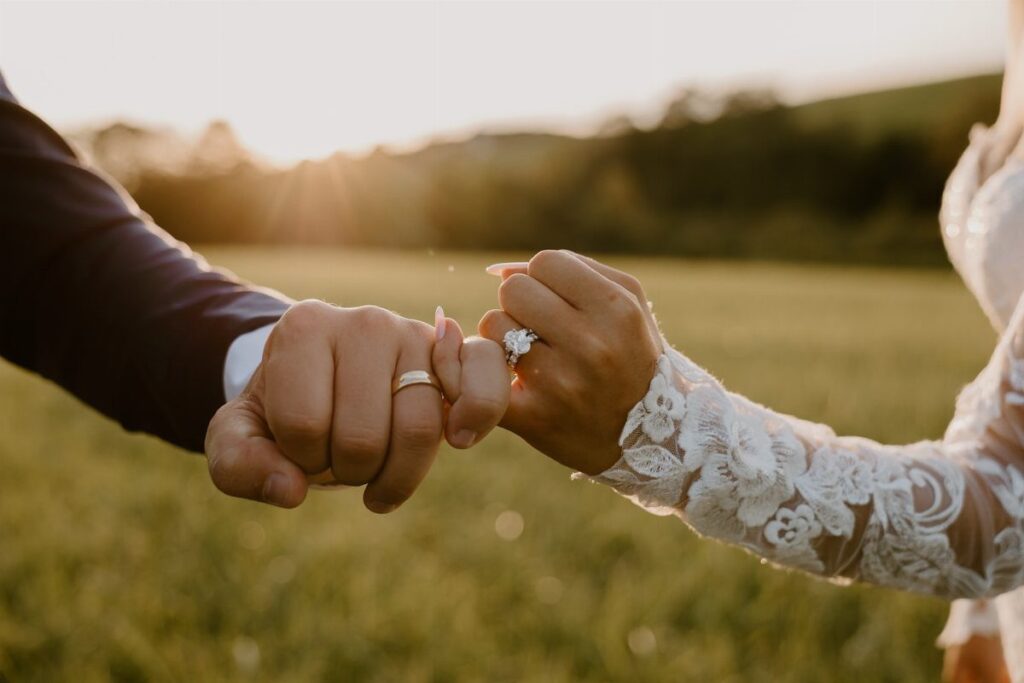 Couple's hands fist bumping showing wedding rings in a sunny outdoor field