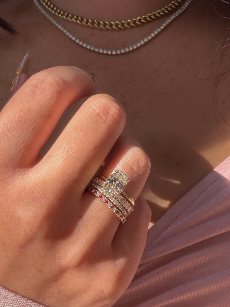 Stacked engagement rings with diamonds and red stones on a woman's finger