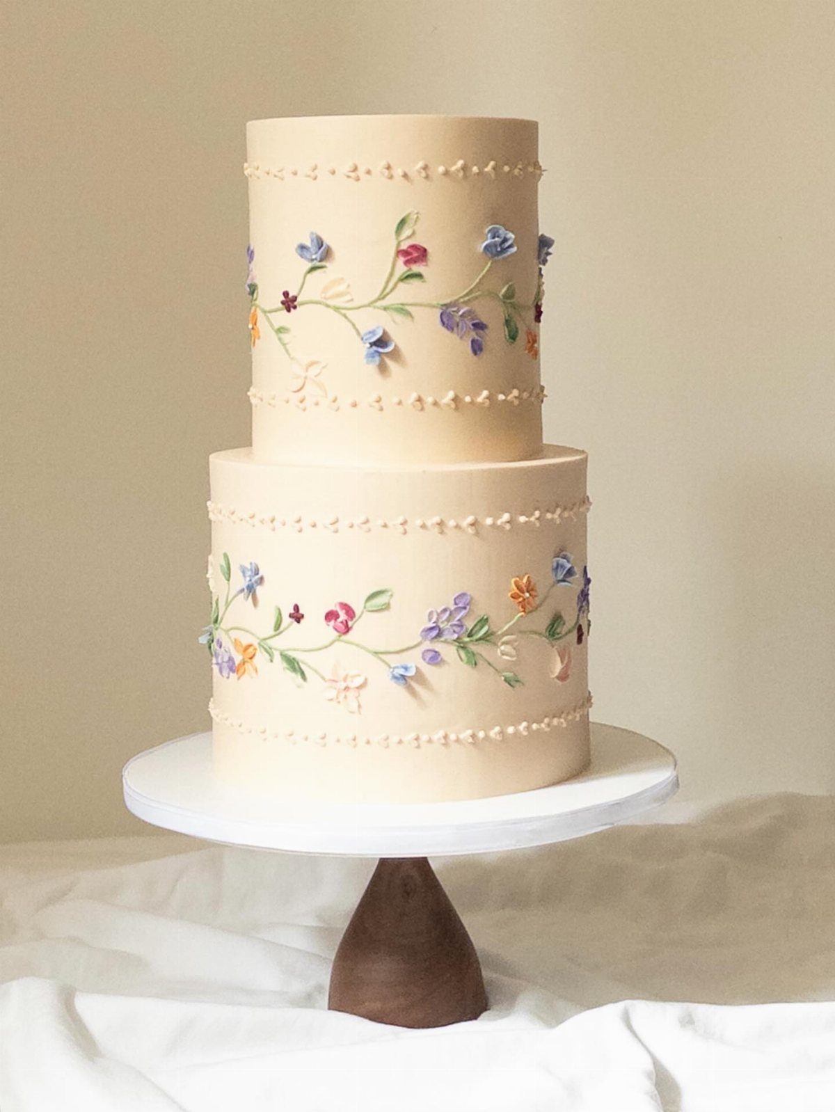 Two-tier white wedding cake decorated with colorful painted spring flowers on a pedestal