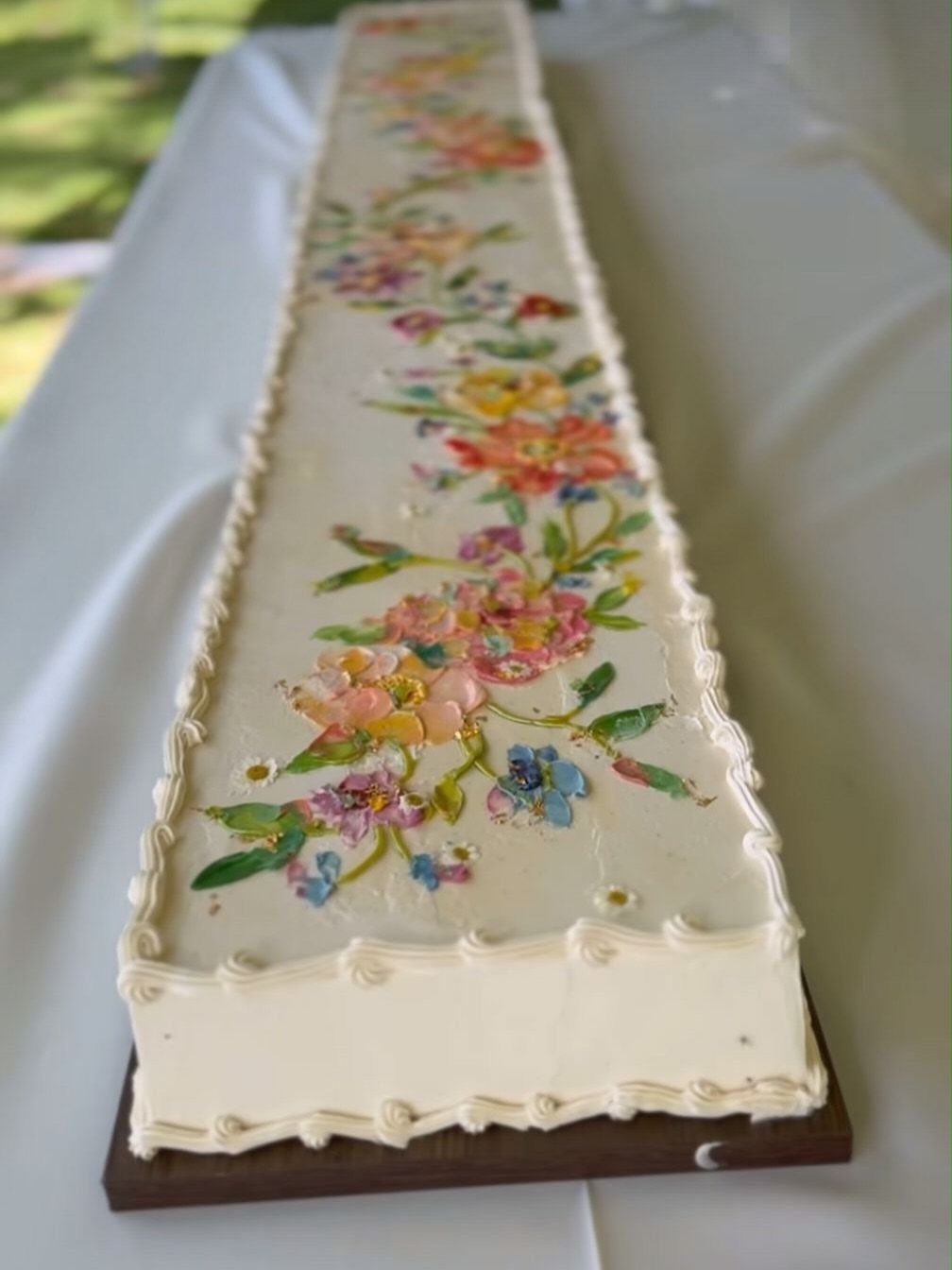 Long white cake decorated with colorful spring floral patterns on a white tablecloth