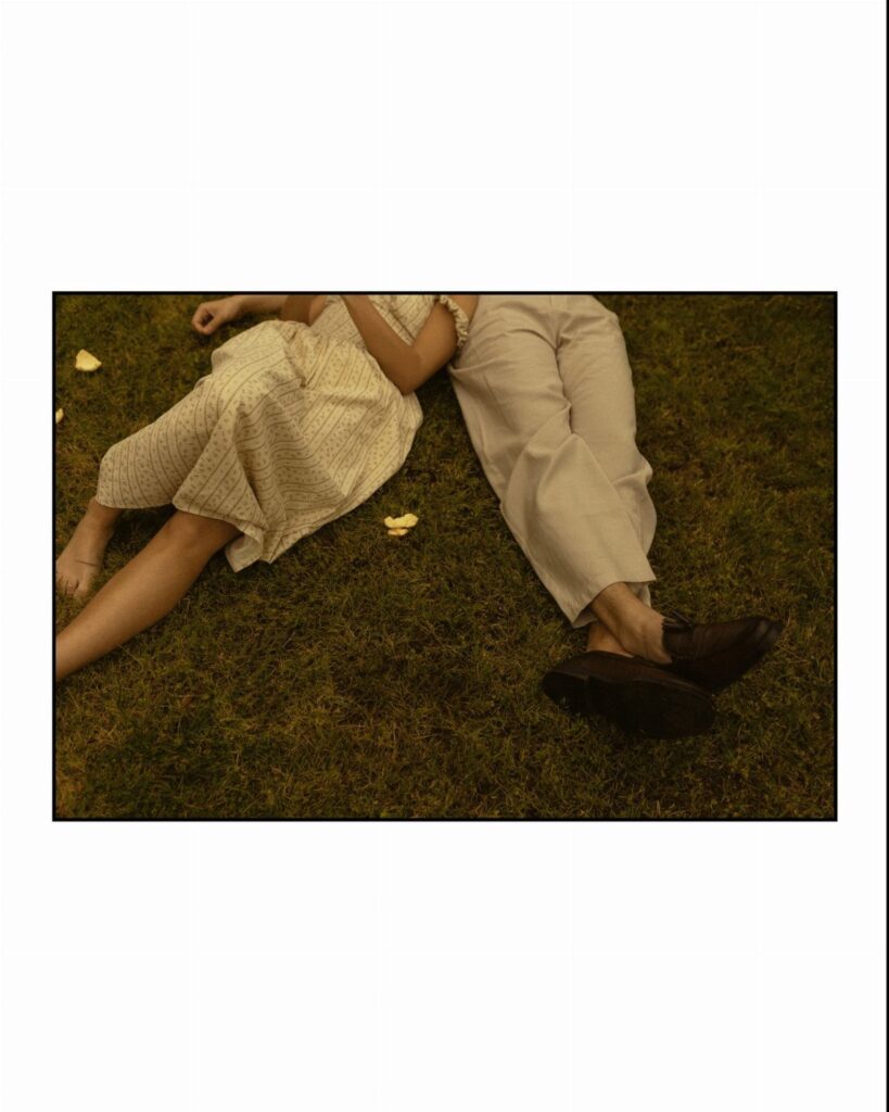 Couple in vintage clothing lying side-by-side on a green grass lawn.