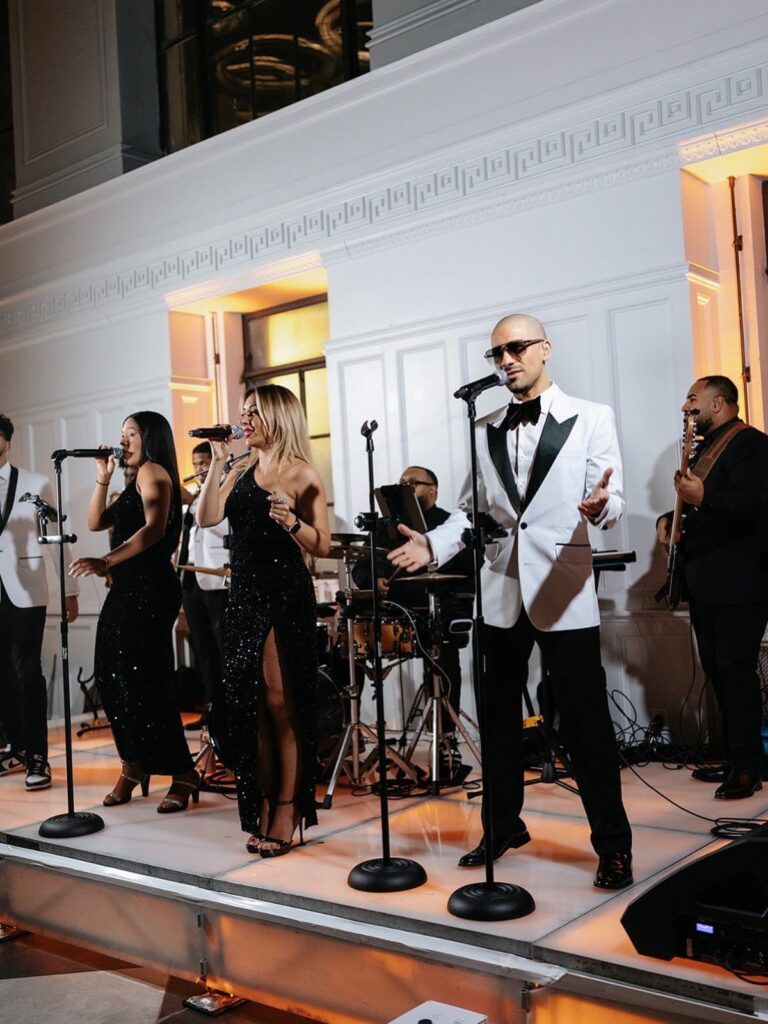 Live musical band with singers and musicians performing on a white stage.
