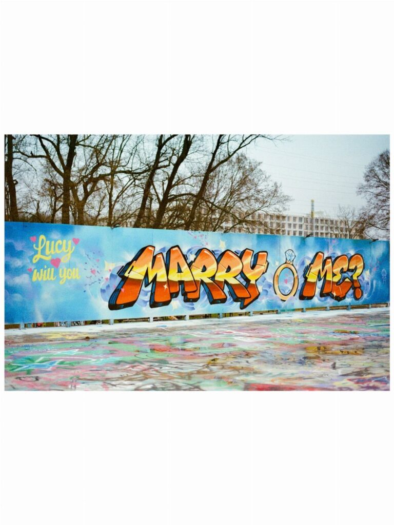 Graffiti wall with colorful letters asking Lucy to marry me in an outdoor setting.